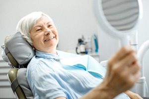 An older woman looks at her smile in the mirror while at the dentist’s office