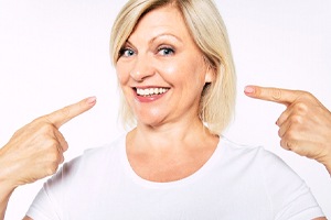 A middle-aged woman wearing a white shirt points at her smile