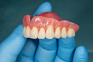 Blue gloved hand holding a full upper arch of dentures