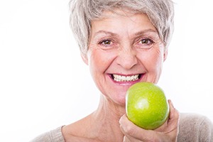Woman with brown eyes holding green apple next to her smile