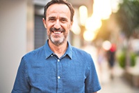 An older man wearing a short-sleeve, button-down shirt and smiling after receiving dental implants