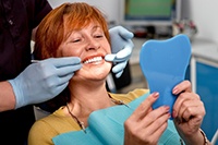 A woman with red hair looks at her smile in the mirror while the dentist shows her the areas of her smile with dental implants