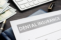 A paper that reads “Dental Insurance” as well as a keyboard, pen, and money all on a table