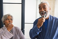 Adult couple smiling while brushing teeth