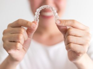 Smiling woman holds up Invisalign in Collierville